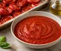 Bowl of smooth red tomato sauce surrounded by oven-roasted tomatoes, garlic and basil