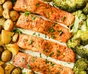 Baked salmon fillets and halved potatoes on a parchment-lined sheet pan with lemon slices