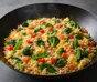 Dark pan filled with fried rice, pieces of egg, spinach, broccoli, red pepper, carrot and snow peas